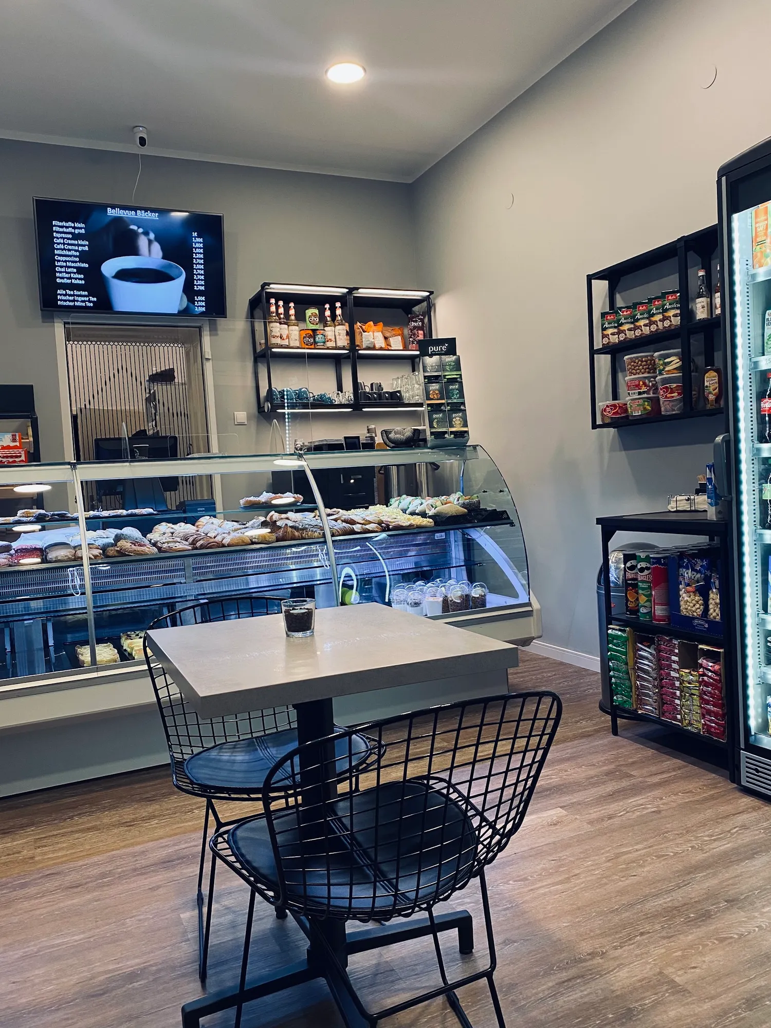 Gastraum mit Drahtstühlen, gefüllter Vitrine und Menütafel