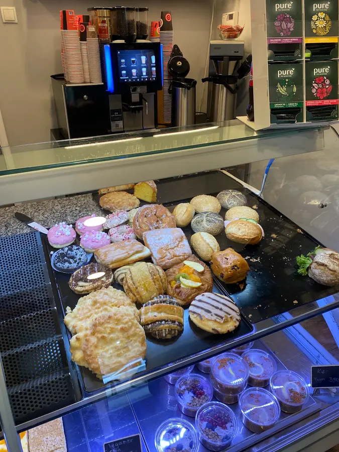 Vitrine mit Donuts, Plundergebäck und Brötchen, dahinter die Kaffeemaschine