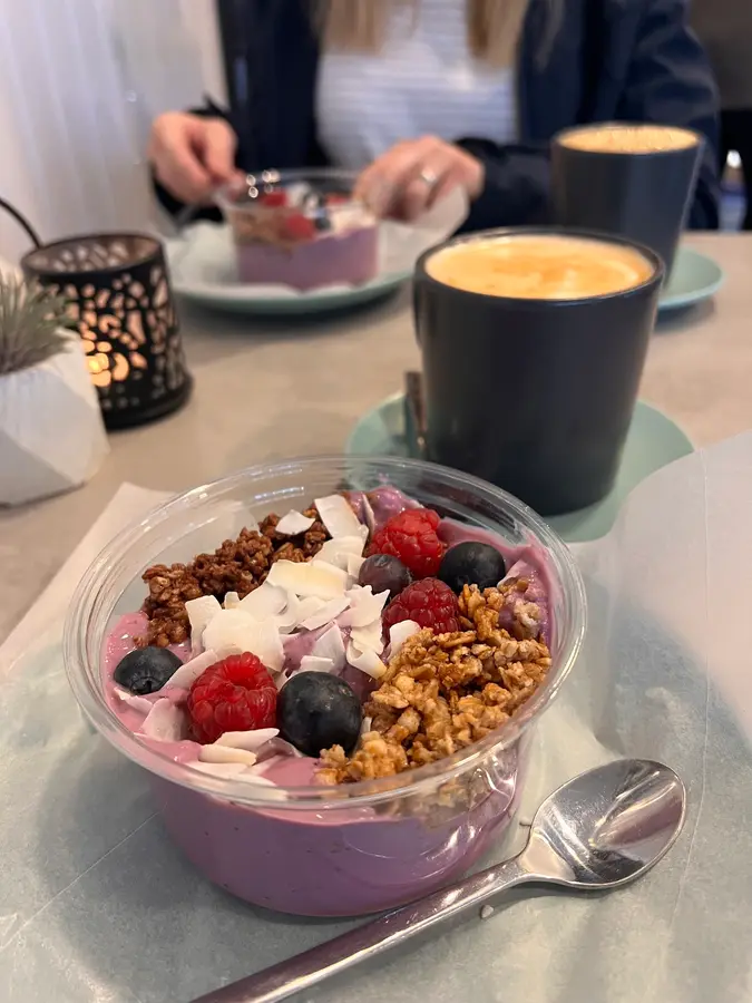 Joghurt-Bowl mit Himbeeren, Blaubeeren, Granola und Kokos, dahinter ein Kaffee