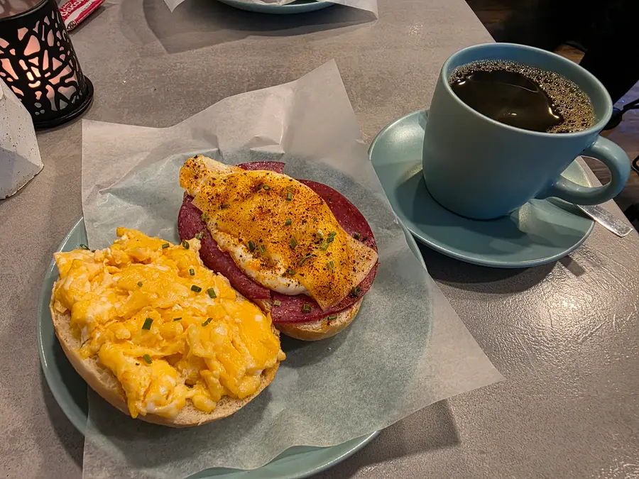 Brötchen mit Rührei und mit Spiegelei auf Salami, daneben ein Kaffee